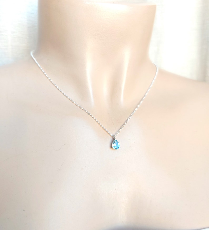 May include: A silver chain necklace with a teardrop-shaped blue gemstone pendant.