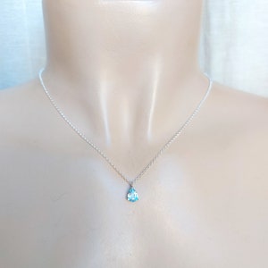 May include: A delicate silver chain necklace with a small teardrop-shaped blue gemstone pendant.