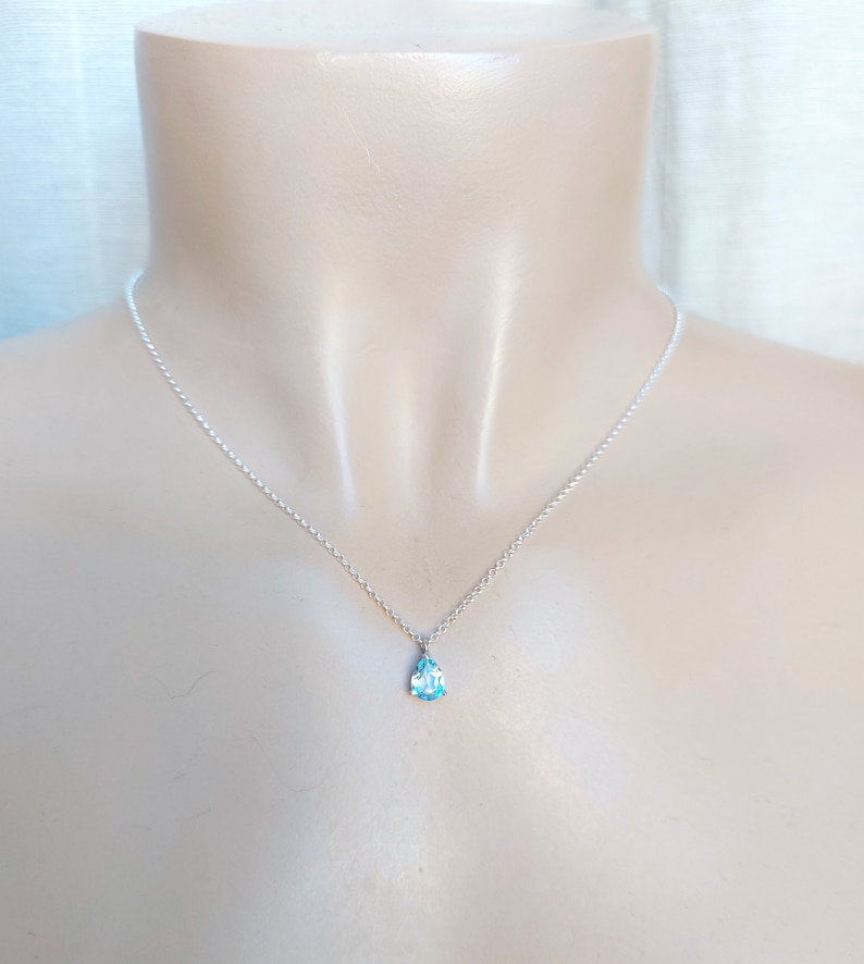 May include: A delicate silver chain necklace with a small teardrop-shaped blue gemstone pendant.