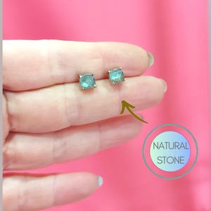 Puede incluir: Un par de pendientes de plata con piedras preciosas verdes de forma cuadrada. Los pendientes están en una mano, y el texto "NATURAL STONE" es visible en la imagen.