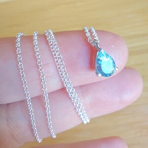 May include: A silver chain necklace with a teardrop-shaped blue gemstone pendant.