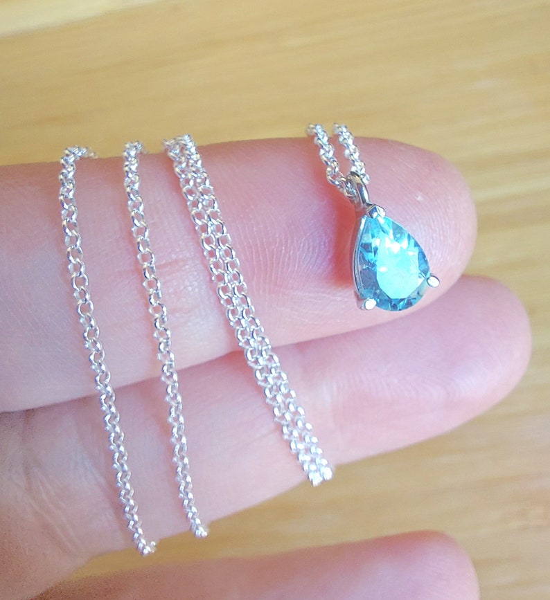 May include: A silver chain necklace with a teardrop-shaped blue gemstone pendant.