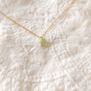 May include: A delicate gold chain necklace featuring a single, small, teardrop-shaped light green gemstone pendant held in a gold prong setting. The necklace is presented as a simple, refined piece of jewelry with a thin, polished gold metal chain.
