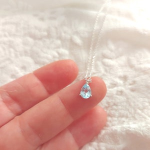 May include: A delicate silver necklace with a teardrop-shaped light blue gemstone pendant.