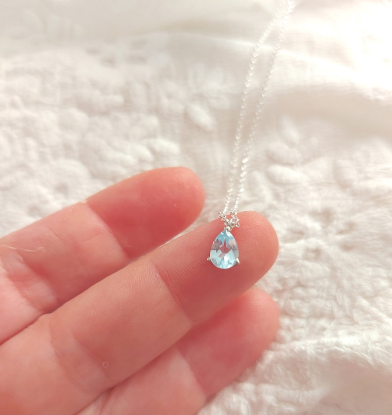 May include: A delicate silver necklace with a teardrop-shaped light blue gemstone pendant.