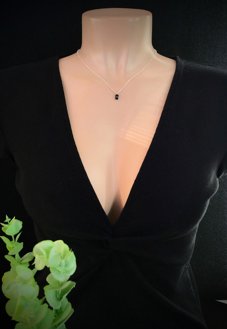 May include: A silver chain necklace with a small black rectangular pendant.