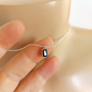 May include: A delicate silver chain necklace with a small rectangular black gemstone pendant.