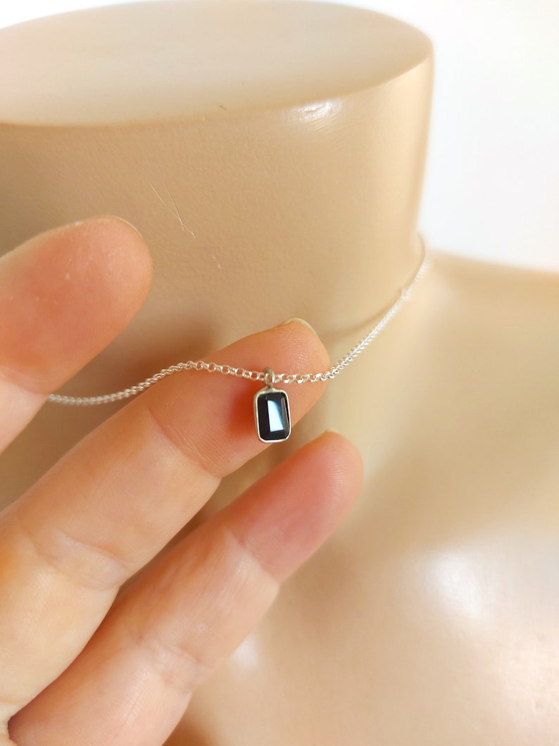 May include: A delicate silver chain necklace with a small rectangular black gemstone pendant.