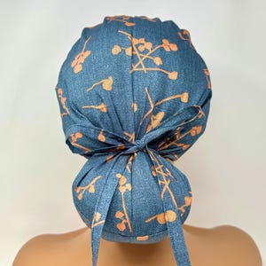 May include: A blue scrub cap with a floral pattern in shades of orange. The cap is tied in a bow at the back. The fabric appears to be denim-like. This cap is designed for medical professionals or those in similar fields.