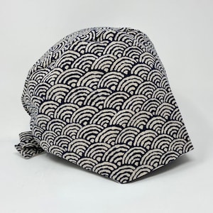 May include: A navy blue and white patterned surgical scrub hat with a tie. The pattern is a repeating design of white waves on a navy blue background.