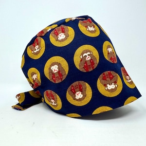 May include: A navy blue head covering with a repeating pattern of monkeys in yellow circles. The monkeys have brown faces and red and brown clothing. The head covering is tied at the back.