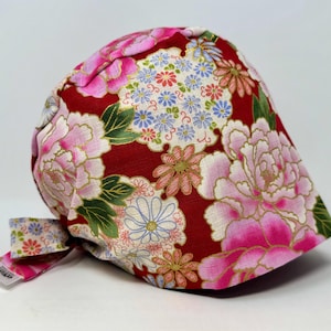 May include: A red fabric cap with a floral pattern featuring pink peonies, blue and white flowers, and green leaves. The cap has a bow on the side and is likely used for medical or culinary purposes.