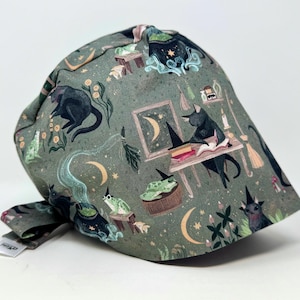 Peut inclure: Un bonnet en tissu vert avec un motif fantaisiste représentant des chats noirs, des lunes, des chaudrons et des grenouilles. Le bonnet a une fermeture à nouer et est probablement destiné à être utilisé dans une cuisine ou comme couvre-chef. Le thème général est Halloween ou la sorcellerie.