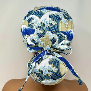 May include: A blue and white patterned scrub cap featuring a Japanese wave design. The cap has a tie closure at the back and is made of a soft fabric. The design includes shades of blue, white, and gold.