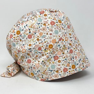 May include: A floral print bonnet. The bonnet is patterned with small flowers in pink, yellow, blue, and orange on a white background. It is tied at the bottom with a matching fabric tie.
