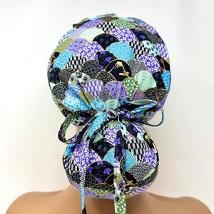 Könnte beinhalten: Eine gemusterte OP-Haube mit japanischem Wellen- und Bergdesign in Blau-, Lila-, Grün- und Schwarztönen. Die Haube hat eine Schleife hinten und Bänder zum Verstellen. Der Stoff hat goldene Akzente.