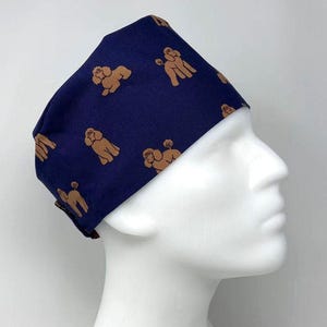 May include: A navy blue surgical scrub cap featuring a repeating pattern of brown poodle illustrations. The cap is made of fabric and is designed to cover the hair during medical procedures or other activities.