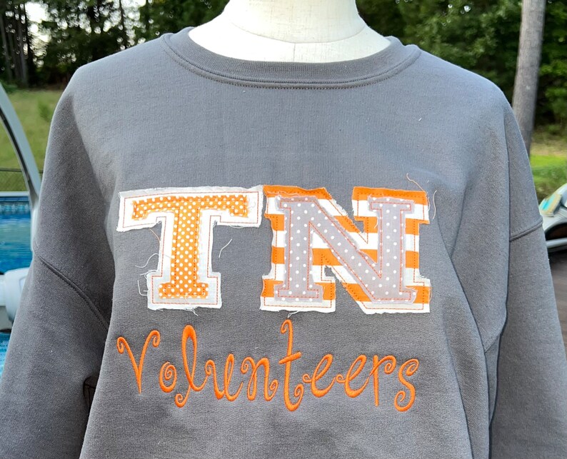 May include: Grey sweatshirt with a large orange and white "TN" appliqu&eacute; and the word "Volunteers" embroidered in orange below.