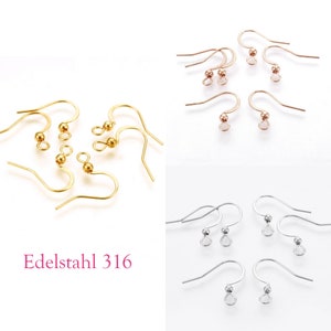 Könnte beinhalten: Eine Auswahl an Ohrhaken in Gold, Roségold und Silber. Die Haken haben ein gebogenes Design mit einem kleinen Ball oder einer Schlaufe am unteren Ende. Der Text "Edelstahl 316" ist rosa gedruckt.