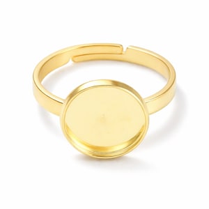 Könnte beinhalten: Ein goldfarbener, verstellbarer Ring mit einer runden Lünettenfassung. Der Ring besteht aus einem glänzenden, metallischen Material und hat ein schlichtes, elegantes Design. Die Lünettenfassung ist für einen runden Stein oder Cabochon gedacht.