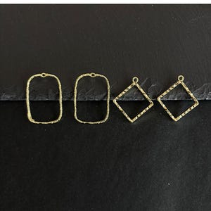 Könnte beinhalten: Vier goldfarbene Metall-Schmuckanhänger. Zwei sind rechteckig mit strukturierten Kanten, und zwei sind rautenförmig mit strukturierten Kanten. Alle haben oben eine kleine Schlaufe zum Befestigen an anderen Schmuckkomponenten. Der Hintergrund ist schwarz.