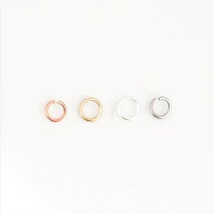 Könnte beinhalten: Drei Sprungringe in verschiedenen Metalloberflächen: Gold, Silber und Roségold.