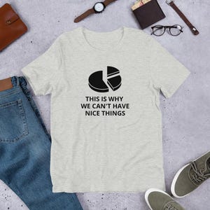 Può includere: T-shirt grigio chiaro con grafica a torta nera e la scritta "THIS IS WHY WE CAN'T HAVE NICE THINGS." La maglietta è realizzata in materiale morbido, adatta per un abbigliamento casual.