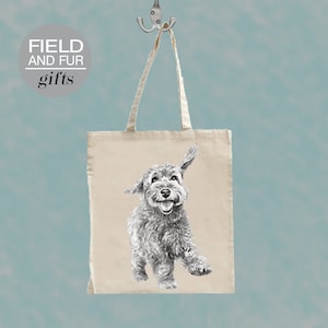 Op de afbeelding: Een witte canvas draagtas met zwarte handvatten. De tas heeft een zwart-witte illustratie van een hond op de voorkant. De tekst "FIELD AND FUR gifts" is in zwart gedrukt op een witte cirkel in de linkerbovenhoek van de tas.
