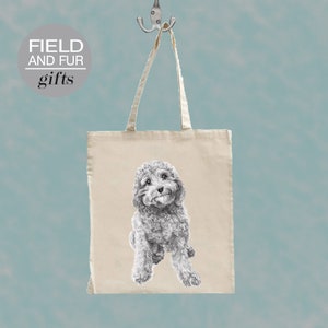 May include: A white canvas tote bag with a black and white illustration of a small dog on the front. The text "FIELD AND FUR gifts" is printed in black on a white circle in the top left corner of the bag.