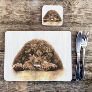 Könnte beinhalten: Ein Platzset und Untersetzer-Set mit einer Aquarellillustration eines braunen Hundes. Der Hund ist mit dem Kopf auf einer Oberfläche dargestellt. Ein Messer und eine Gabel befinden sich rechts vom Platzset. Das Set ist für den Essbereich.