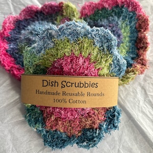 May include: Three colorful, handmade dish scrubbies made of 100% cotton. The scrubbies are round and have a textured, fluffy surface. The scrubbies are labeled "Dish Scrubbies Handmade Reusable Rounds 100% Cotton".