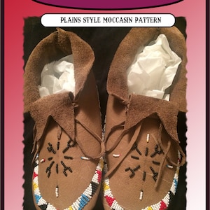 May include: A pair of brown leather moccasins with intricate beadwork. The moccasins have a geometric pattern of black, white, red, blue and yellow beads. The text "PLAINS STYLE MOCCASIN PATTERN" is visible above the moccasins.