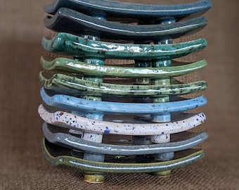 May include: A stack of nine ceramic dishes in various shades of blue, green, and white. The dishes are glazed and have a speckled finish. They are stacked on top of each other, creating a decorative display.