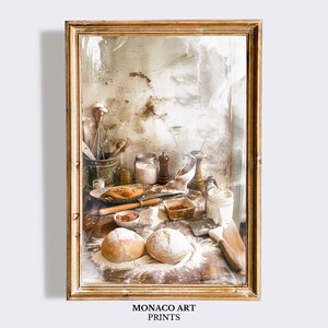 May include: A framed art print titled MONACO ART PRINTS featuring a rustic kitchen scene with two round loaves of bread, scattered flour, a wooden rolling pin, a small bowl of cocoa powder, a metal whisk, and various glass jars on a wooden surface.