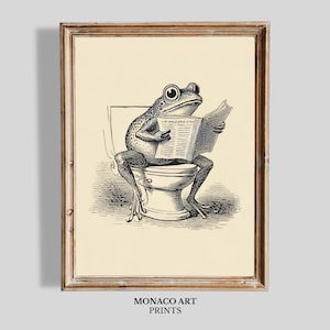 May include: A framed wall art print featuring a black and white line drawing of a frog sitting on a toilet while reading a newspaper. The illustration is set against a cream-colored background. The text MONACO ART PRINTS appears below the frame.