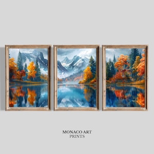 May include: A triptych of framed wall art prints featuring a landscape of snow-capped mountains, a calm lake, and autumn trees with vibrant orange and yellow foliage. The reflection of the trees and mountains is visible in the water. Text reads MONACO ART PRINTS.