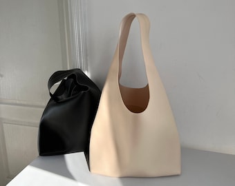 May include: Two leather tote bags, one in black and one in a light beige color. The bags are sitting on a white surface.