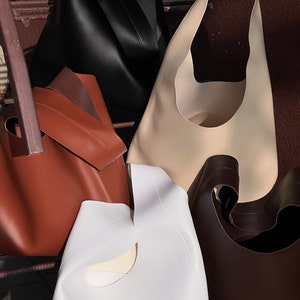 May include: Four different leather tote bags in various colors, including black, brown, white, and beige. The bags have a unique cut-out design on the front.