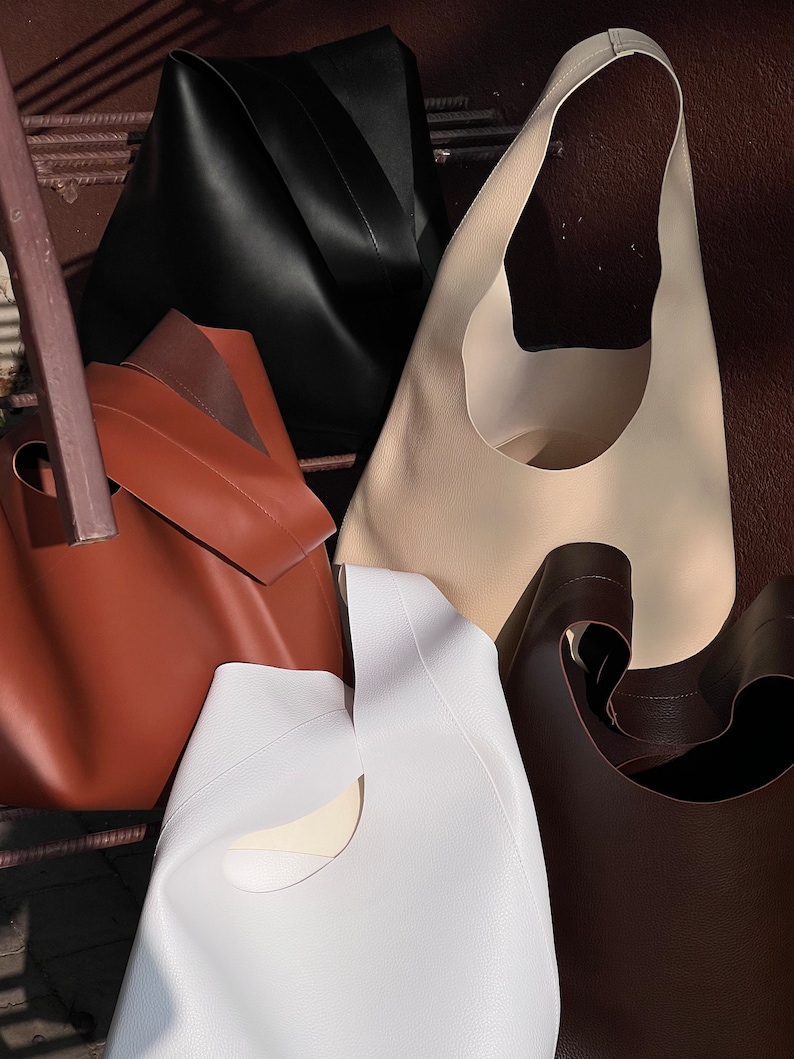 May include: Four different leather tote bags in various colors, including black, brown, white, and beige. The bags have a unique cut-out design on the front.