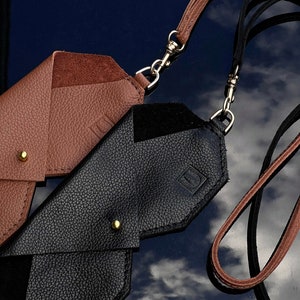 May include: Two leather phone cases with straps. One case is brown and the other is black. Both cases have a gold metal clasp.