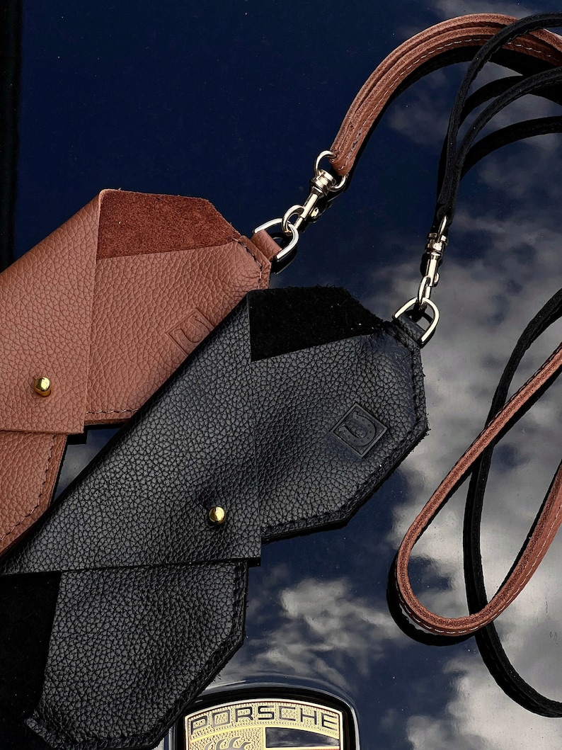 May include: Two leather phone cases with straps. One case is brown and the other is black. Both cases have a gold metal clasp.