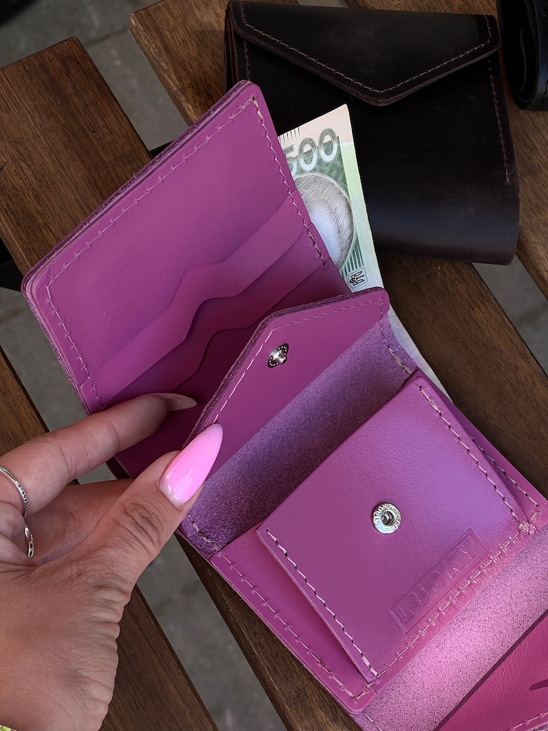 May include: A pink leather wallet with a snap closure and the word "LUSTY" embossed on the front. The wallet is open and shows multiple compartments for cards and cash.