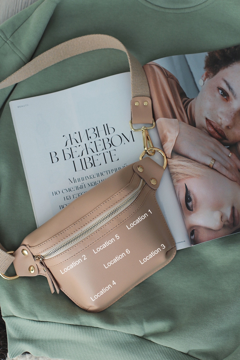May include: A beige leather fanny pack with a gold zipper and buckle. The fanny pack has six numbered locations on the front.
