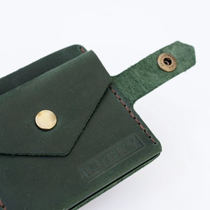 May include: A dark green leather wallet with a flap pocket and a snap closure. The wallet has a brown stitched edge and the word "LUCKY" embossed on the front.
