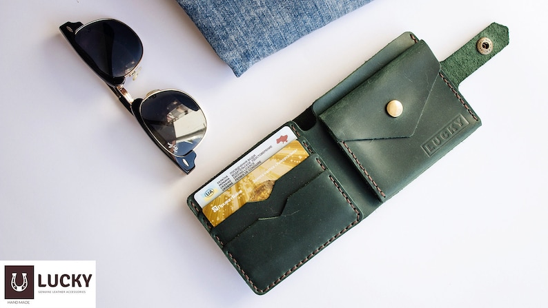 May include: A green leather wallet with a flap closure and a snap button. The wallet has a card slot and a pocket for cash. The wallet is embossed with the word "LUCKY".