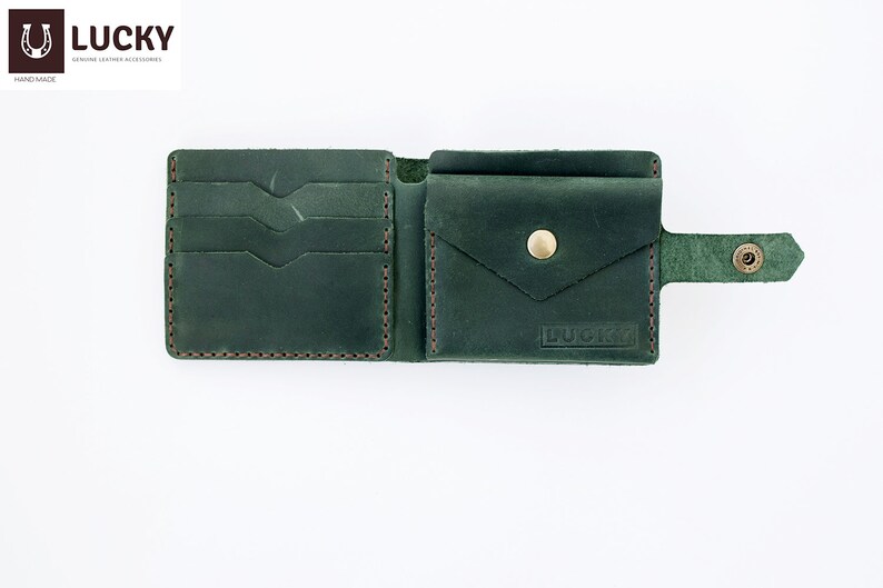 May include: A dark green leather wallet with multiple card slots, a billfold, and a flap pocket. The wallet has a snap closure and a small strap with a button. The wallet is embossed with the word "LUCKY".