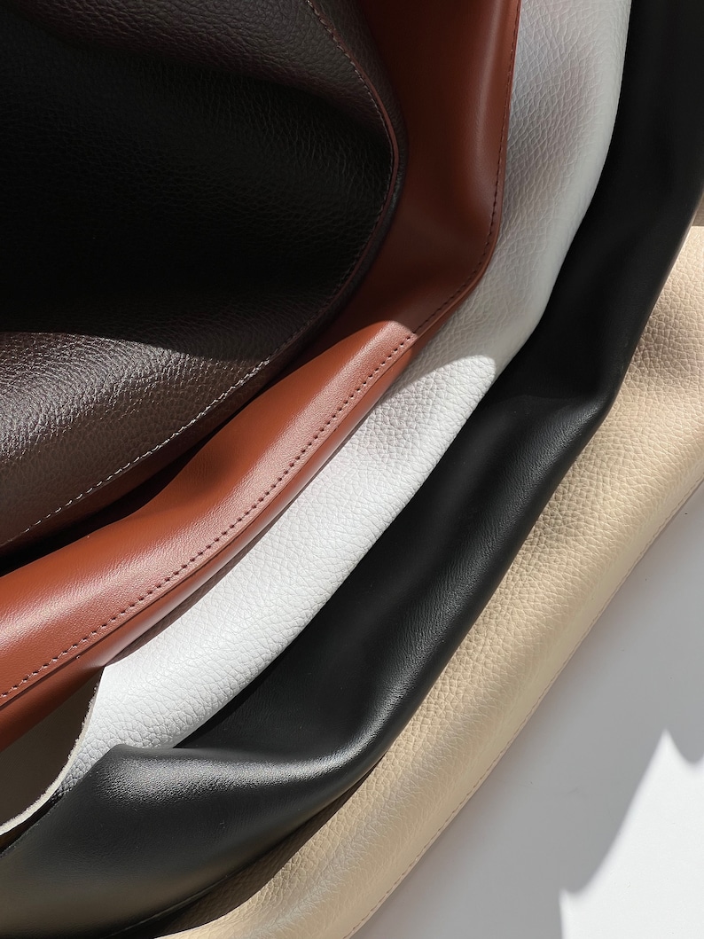 May include: Close-up of four different types of leather in brown, tan, white, and black. The leather is textured and has a soft, supple feel.