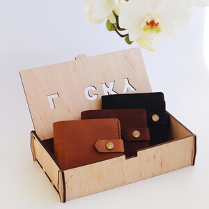 May include: Three leather wallets in a wooden box with the word "Г С К Л" engraved on the lid. The wallets are brown, dark brown, and black.