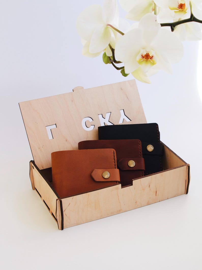 May include: Three leather wallets in a wooden box with the word "Г С К Л" engraved on the lid. The wallets are brown, dark brown, and black.