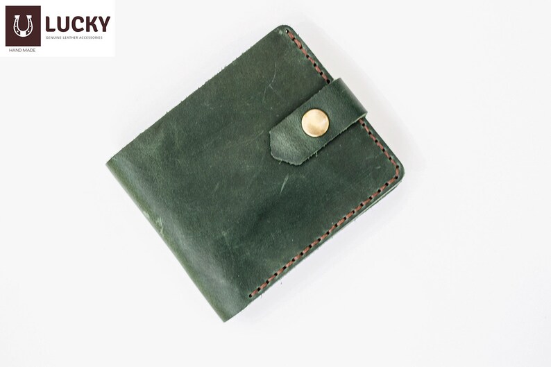 May include: A dark green leather wallet with a brown stitch detail and a gold button closure. The wallet has a flap closure with a strap.